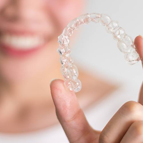 Smiling patient holding clear aligner