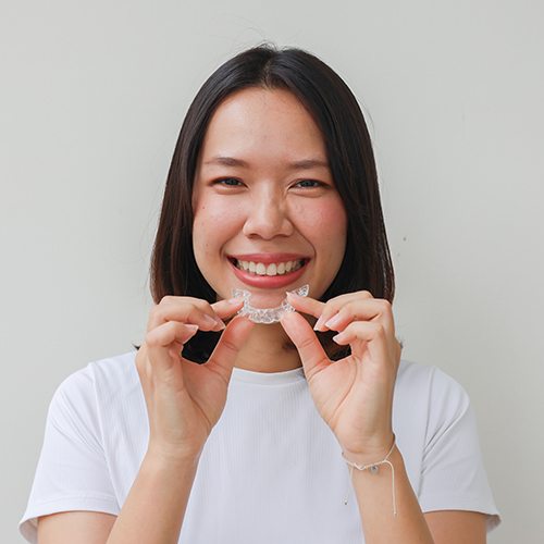 Woman smiling while holding Invisalign aligner